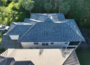 A two-story suburban home with a light-gray asphalt shingle roof, viewed from the front yard, surrounded by trees and lush landscaping under a vibrant blue sky—highlighting the home's refreshed roofing in Land O Lakes, FL