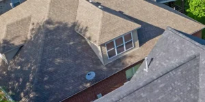 Wide shot of a house with a new dark gray shingle roof under clear blue skies, representing high-quality roofing services with a clean, professional finish.